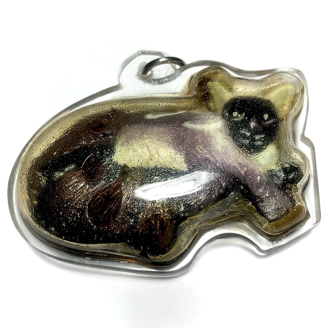 "Noo Kin Nom Maew (Dtua Kroo)," which is part of a Necromantic collection. The amulet features an image of a mouse drinking from a cat's teat, and it's infused with Prai Oil, a substance used in Thai spiritual practices. Two Takrut (spells) are included, along with an enchanted coin and dice. The amulet was created, blessed, and empowered by Kroo Ba Porn, a Thai Lanna Master Sorcerer-Monk from Wat Phu Or Temple in Chiang Mai, Thailand.